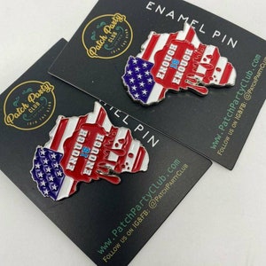 May include: Two enamel pins in the shape of a map, featuring the American flag design with red and white stripes, blue stars, and the words "ENOUGH IS ENOUGH." The pins are on black cards with the "Patch Party Club" logo.