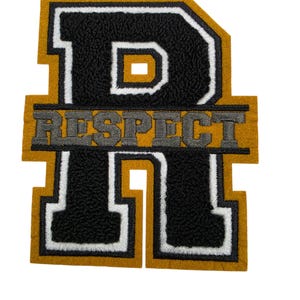 Puede incluir: Un parche con la letra R de estilo universitario que presenta un centro negro texturizado con un borde blanco y un contorno amarillo mostaza. La palabra RESPECT está bordada en letras grises sobre una barra horizontal de color mostaza.