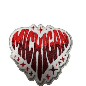 Könnte beinhalten: Ein herzförmiger Stickaufnäher mit dem Wort MICHIGAN in einem rot-dunkelroten Farbverlauf. Das Design enthält kleine rote Sternakzente und einen weißen Rand, wobei die Buchstaben in einer tropfenden, flüssigkeitsähnlichen Optik gestaltet sind.