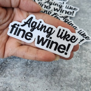 May include: White iron-on patch with black embroidery that reads "Aging like fine wine!"