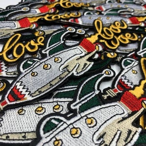 May include: A collection of embroidered patches featuring a cartoon submarine with the word "love" in yellow thread. The submarine is gray with red and white accents. The patches are on a white background.