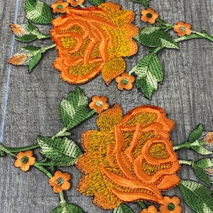 May include: Two embroidered floral patches featuring large orange and yellow roses with green leaves and small orange flowers. The patches are detailed with intricate stitching and are ideal for fabric embellishment.