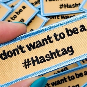 Puede incluir: Un parche de tela beige y azul claro con el texto "No quiero ser un #Hashtag" en negro.