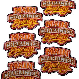 Puede incluir: Cinco parches bordados idénticos que presentan el texto "MAIN CHARACTER Energy" en una fuente negrita y superpuesta. Las letras son de color naranja y amarillo con un contorno rojo oscuro y un borde negro, creando un aspecto vibrante y multicolor.