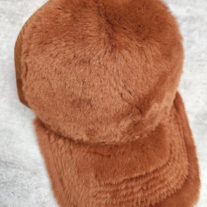 May include: A brown faux fur trucker hat with a mesh back panel. The hat has a curved brim and is made of soft, plush material.