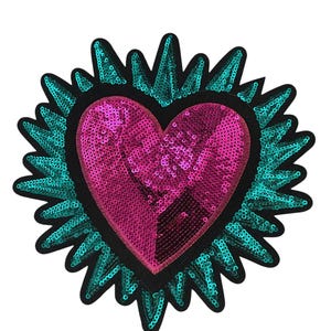 May include: A heart-shaped sequin patch with a pink center and a teal, spiky border. The heart is outlined in black. This decorative patch can be sewn or ironed onto clothing or accessories.