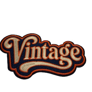 Puede incluir: Un parche bordado que presenta la palabra Vintage en una fuente cursiva. Las letras son de color beige claro con un contorno azul marino oscuro y un borde naranja vibrante, creando un efecto de capas sobre la tela de fondo azul marino.