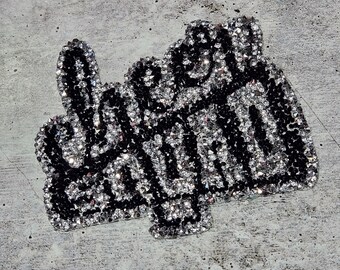 May include: A black and silver iron-on patch with the word "Queen" in rhinestones. The patch is shaped like a hand giving the middle finger.