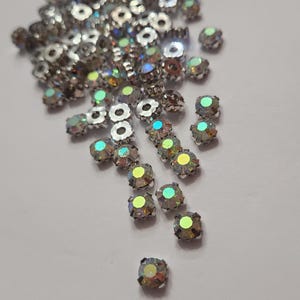 Peut inclure: Un ensemble de strass irisés et facettés avec des montures en métal argenté. Les strass ont une forme carrée avec une monture circulaire et reflètent un arc-en-ciel de couleurs. Ces embellissements décoratifs sont parfaits pour l'artisanat et la bijouterie.