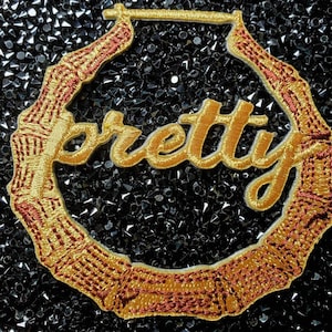 May include: Gold hoop earrings with a red and gold bamboo design and the word "pretty" embroidered in gold.