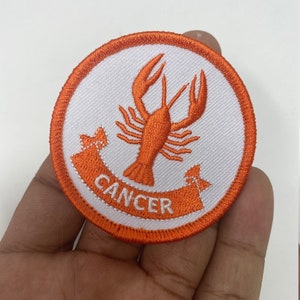 May include: Orange and white embroidered iron-on patch with a crab and the word "Cancer" in a banner.