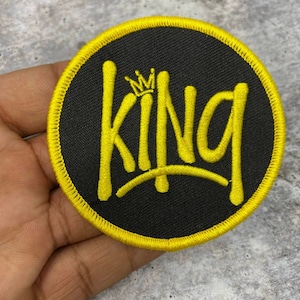 May include: A round black patch with a yellow embroidered border and the word "KING" in yellow with a small crown above the K.