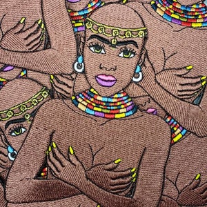 May include: Embroidered patch featuring three women with brown skin, wearing colorful beaded necklaces and headbands. The women are embracing each other, with their arms wrapped around each other's bodies.