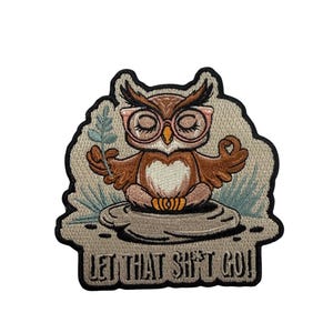 May include: An embroidered patch featuring a brown owl with pink glasses sitting in a lotus position on a gray stone. The owl holds a small green sprig. The background is light beige with green grass accents and the text LET THAT SH*T GO!