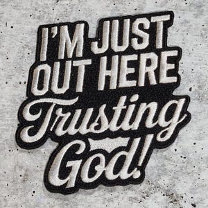 May include: Black and white embroidered patch with the text "I'm just out here trusting God!" in a white cursive font.