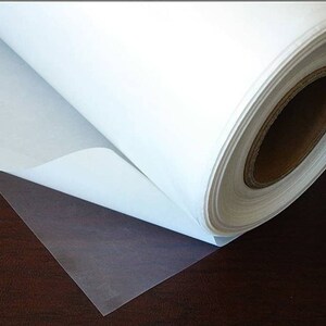 May include: A roll of white adhesive-backed vinyl, partially unrolled, revealing a clear adhesive backing. The vinyl is rolled on a cardboard core.