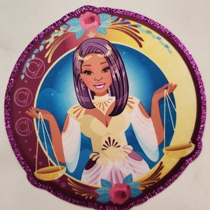 Op de afbeelding: Een ronde, paars omzoomde patch met een kleurrijke illustratie van een vrouw met paars haar die een weegschaal vasthoudt. De vrouw draagt een gele jurk en een kroon. De achtergrond is een blauwe lucht met sterren en een halve maan.