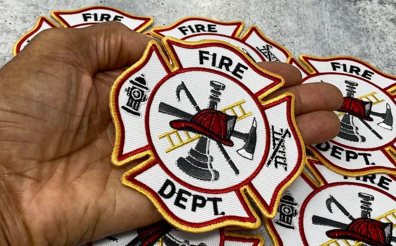 Op de afbeelding: Een witte, rode en gouden brandweerpatch met een brandkraan, een bijl, een ladder en een helm in het midden. De patch zegt "FIRE DEPT."