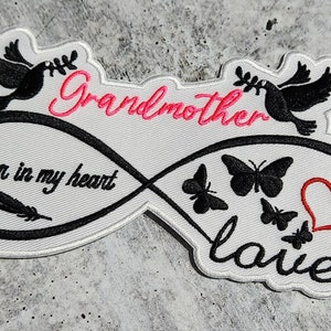Könnte beinhalten: Weißer gestickter Aufnäher mit einem Unendlichkeitszeichen, zwei Tauben, Schmetterlingen und einem Herzen. Der Text lautet "Grandmother forever in my heart love".