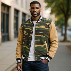 May include: A camouflage bomber jacket with tan sleeves and a white and black striped collar and cuffs. The jacket has a button-up front and two front pockets. The person is wearing a white t-shirt and blue jeans.