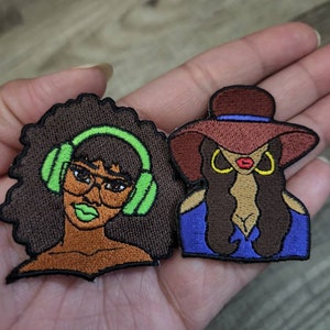May include: Two embroidered iron-on patches featuring women with different hairstyles and accessories. One woman has an afro and is wearing headphones and glasses. The other woman has long hair and is wearing a hat and earrings.