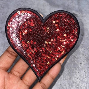 May include: A red heart-shaped patch covered in sequins with a black border.