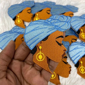 May include: A set of blue and brown embroidered iron-on patches featuring a woman with a blue turban. The woman has brown skin and closed eyes. The patches are perfect for adding a touch of style to clothing, bags, or other accessories.