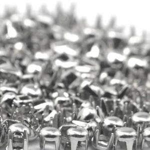 May include: A large collection of small, silver-colored metal studs with rounded tops and four prongs extending from the base. These metallic fasteners are arranged in a dense pile, showcasing their reflective, polished surface and uniform shape.