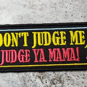 May include: Black embroidered patch with yellow and red text that reads "Don't Judge Me, Judge Ya Mama!" with colourful lightning bolts on either side.