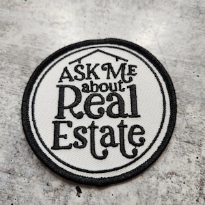 May include: White round patch with black stitching and the text "Ask Me about Real Estate" in black cursive font.