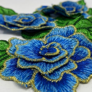 May include: Embroidered blue rose patches with gold trim and green leaves. The floral patches feature detailed stitching and are suitable for various craft projects. The patches are a vibrant blue color with gold accents.