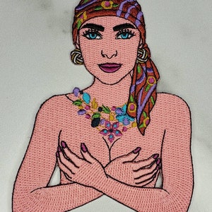 May include: Embroidered patch depicting a woman with a colourful headscarf and a floral necklace. She is wearing a pink top and has her arms crossed over her chest.