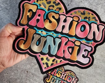 Puede incluir: Dos parches bordados para planchar en forma de corazón con el texto "Fashion Junkie" en una fuente retro colorida. El parche más grande tiene un fondo de estampado de leopardo.