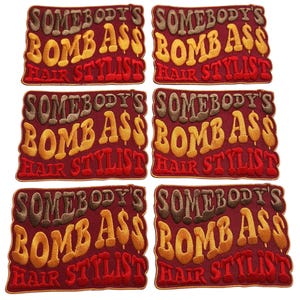 Puede incluir: Seis parches bordados con el texto "SOMEBODY'S BOMB ASS HAIR STYLIST" en hilo marrón, amarillo y naranja sobre un fondo granate. Los parches son rectangulares con esquinas redondeadas.