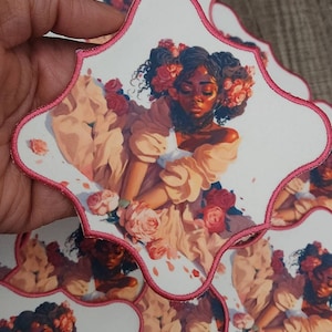 May include: A white patch with a pink border features a digital illustration of a woman with dark skin, brown eyes, and curly hair. She is wearing a white dress with a floral pattern and a crown of pink roses. The background is a light pink with white petals.