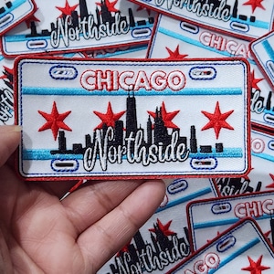 May include: A white and blue embroidered patch with the text "CHICAGO NORTHSIDE" and a black silhouette of the Chicago skyline. The patch features three red stars and a blue and white striped border.
