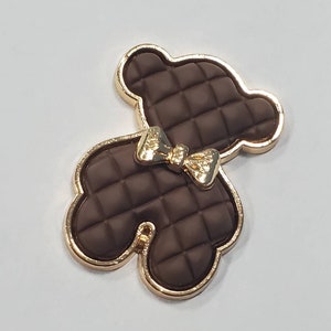 Op de afbeelding: Een bruine, gestikte berenbedel met een gouden strik en gouden rand.