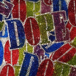 May include: A close-up of a colorful assortment of fabric patches, each featuring a single letter in a different color. The letters are made of rhinestones and are arranged in a random pattern. The patches are perfect for adding a touch of sparkle and personality to any project.