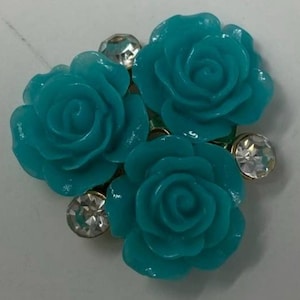 Op de afbeelding: Drie turquoise blauwe plastic rozen met strass accenten.