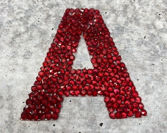 May include: The letter A is formed using red rhinestones on a gray background.