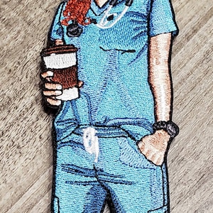 May include: Embroidered patch of a medical professional in blue scrubs, holding a coffee cup. The patch features a stethoscope and red hair. The design is detailed with various shades of blue and brown.