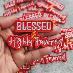 May include: Red and white embroidered patches with the words "BLESSED & Highly Favored". The patches have a rectangular shape with white text on a red background. Several patches are scattered.