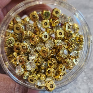 Peut inclure: Gros plan sur un bocal en verre transparent rempli de strass carrés dorés et transparents.