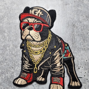 Puede incluir: Parche bordado de un bulldog francés con una chaqueta de cuero negra, gafas de sol rojas, una cadena de oro y una gorra de béisbol roja y negra con las letras "KGF" en ella.