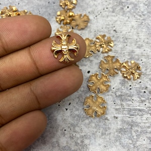 May include: A close-up of a gold-colored metal cross with a skull design. The cross is surrounded by several other gold-colored metal crosses.