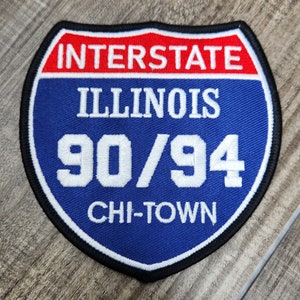 May include: A blue and red embroidered patch with the text "INTERSTATE ILLINOIS 90/94 CHI-TOWN"