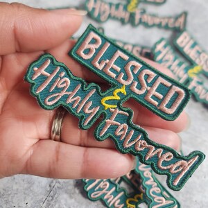 May include: A set of green and pink embroidered iron-on patches with the text "Blessed & Highly Favored".
