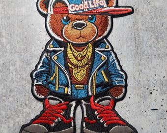 Puede incluir: Parche bordado de un osito de peluche que lleva una chaqueta vaquera azul, pantalones vaqueros, zapatillas rojas y una gorra de béisbol azul y roja con el texto "Good Life" en ella.