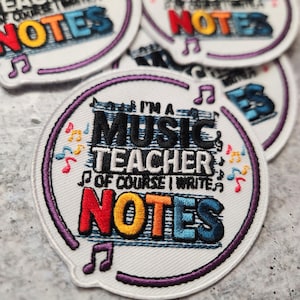May include: White embroidered patch with purple stitching. The patch features a musical note design and the text "I'm a Music Teacher, of course I write notes".