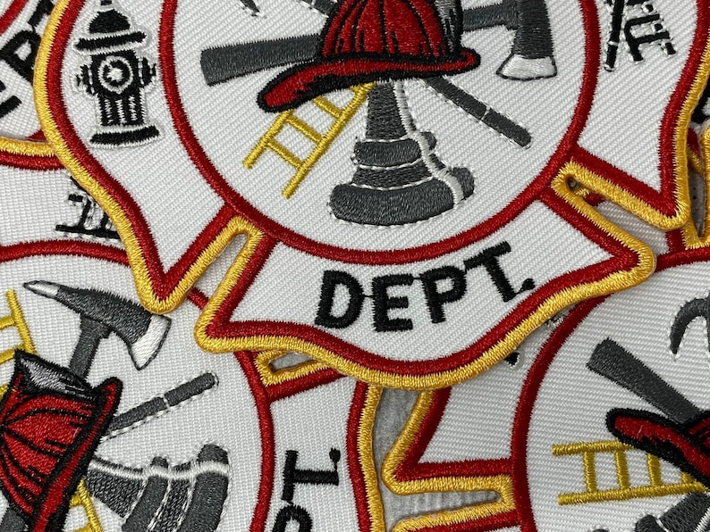 Op de afbeelding: Close-up van drie geborduurde patches met een brandweerthema. De patches zijn wit met rode en gouden randen. De middelste patch heeft een brandkraan, een bijl en een ladder. De tekst "DEPT." is in het zwart geborduurd aan de onderkant van de patch.